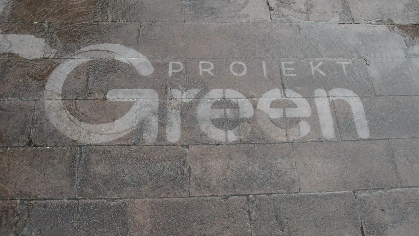 Mensaje de Green Proiekt visible sobre el pavimento mojado.